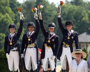 Young dressage riders triumphantly hold their bouquets aloft as they accept their team gold medals.